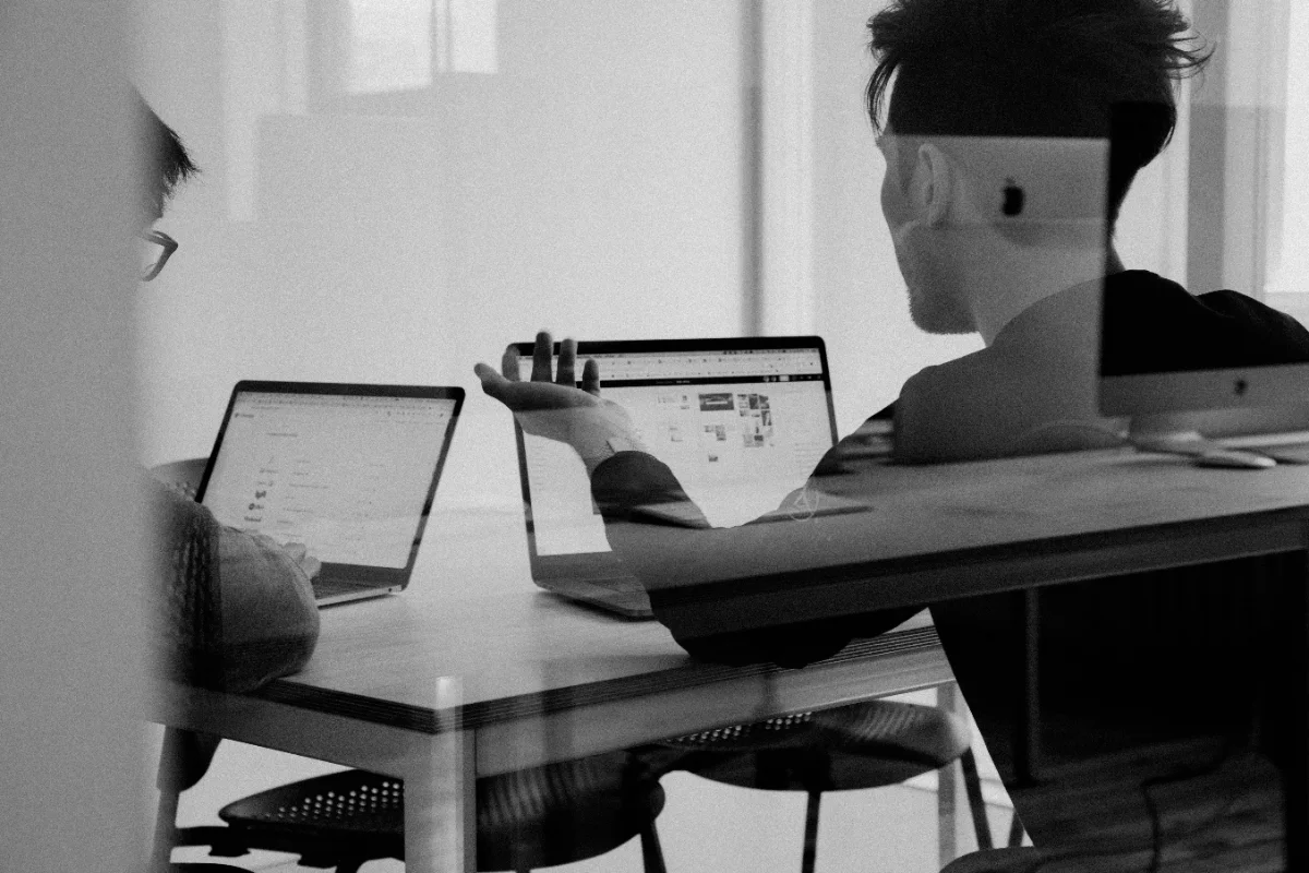 Two people working at laptops, seen through a glass partition.